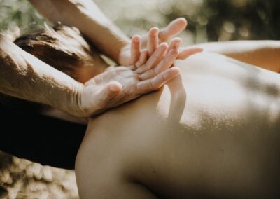 Masaż zewnętrzną stroną rąk pleców kobiety na wysokości barków, technika masażu lomi lomi nui.
