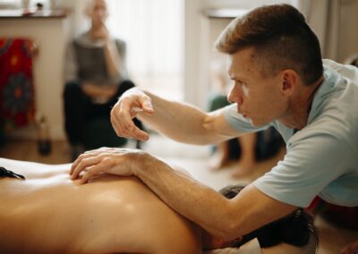 Na pierwszym planie Piotr Blue prowadzi instruktaż. Drugi plan uczestnik kursu masażu lomi się przygląda