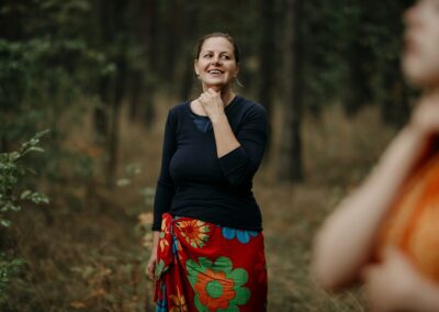 Kobieta trzyma rękę na gardle, stoi w lesie.