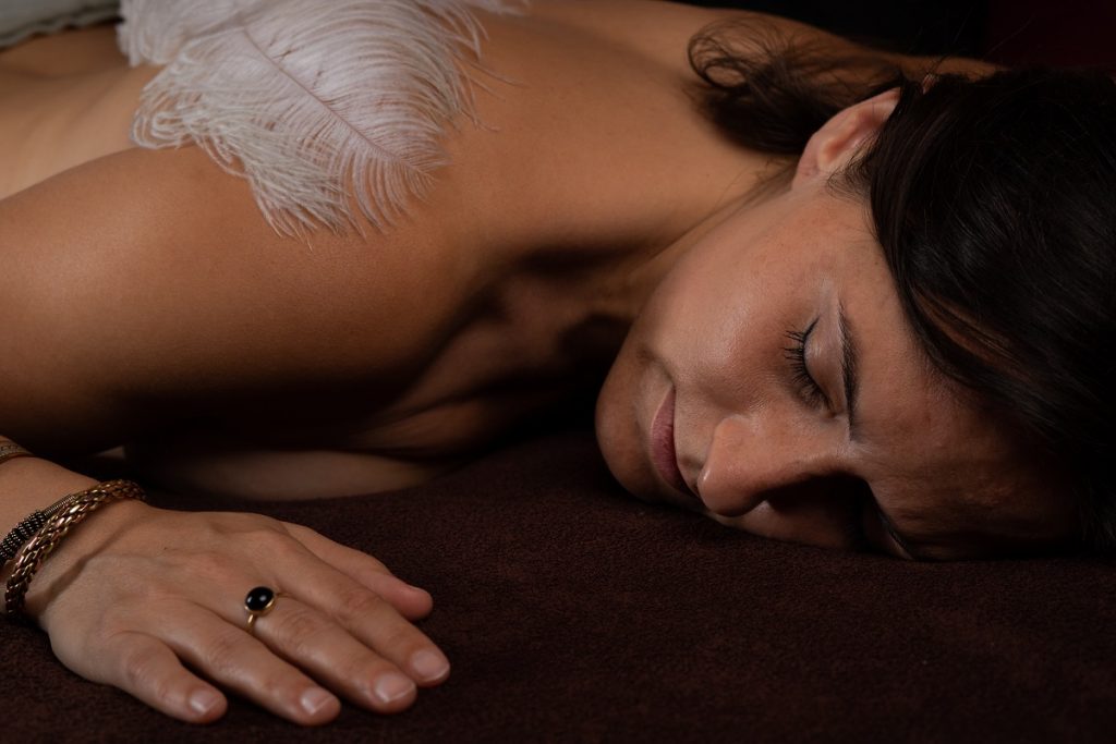 Kobieta jest masowana piórkiem podczas masażu tantrycznego