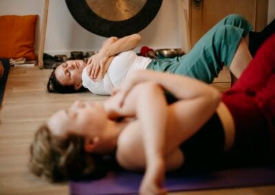 Two women lie on a mat and perform breathing exercises during the lomi lomi course.