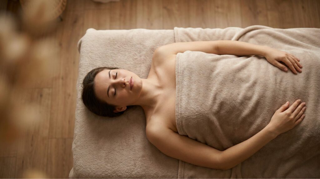 Osoba leżąca na macie do masażu, widoczna z góry, spokojny wyraz twarzy, dłonie ułożone wzdłuż ciała, klimat skupienia i bezpieczeństwa